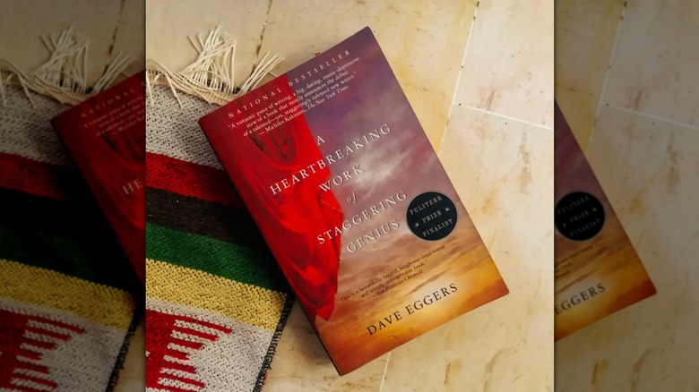 A copy of "A Heartbreaking Work of Staggering Genius" laying on a tile floor and the corner of a rug