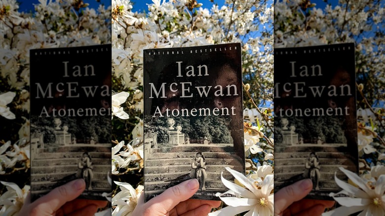 A hand holding up "Atonement" by Ian McEwan in front of a flowering tree