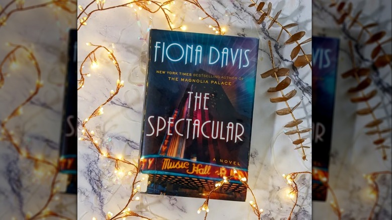 A copy of "The Spectacular" on a table with string lights