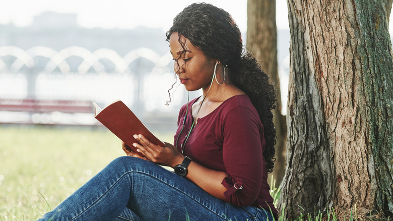 Woman sitting in the grass against a tree reading