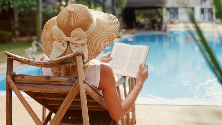 Person in a hat with a bow reading by the pool