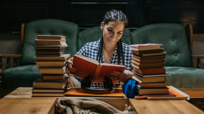 Woman sitting at a table with stacks of books, reading one