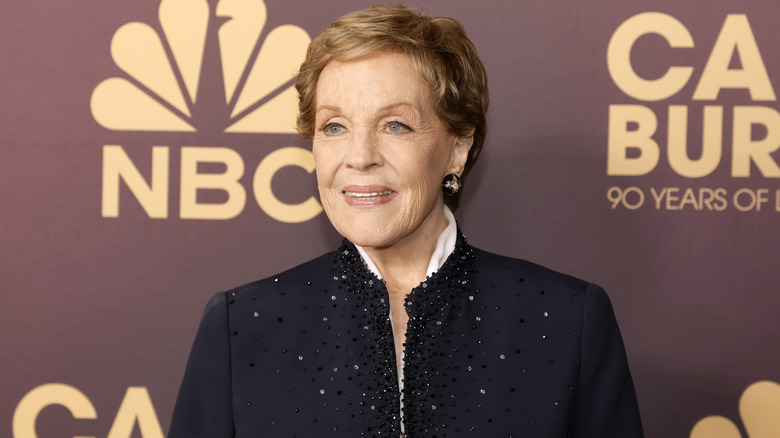 Julie Andrews smiling at a 2023 NBC event while wearing a blue jacket decorated with sparkles