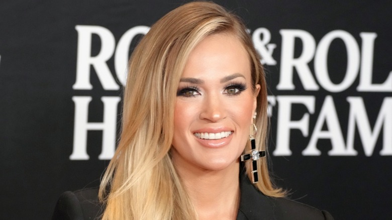 Carrie Underwood smiling with her hair over her right shoulder, posing in front of a black background