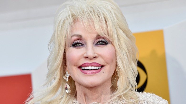 Dolly Parton smiling on the red carpet in front of a white, yellow, and orange background
