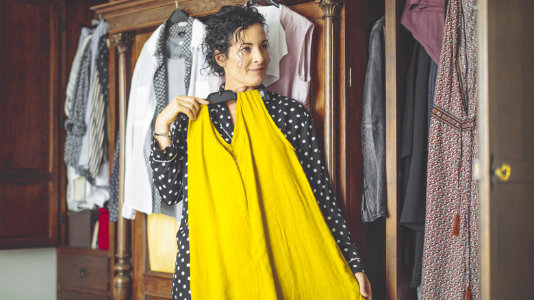 Woman holding yellow jumpsuit up to herself looking in a mirror