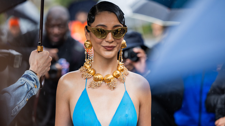 Fashion week attendee wearing chunky statement jewelry and gold sunglasses