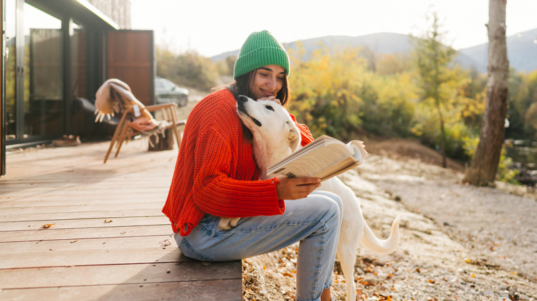 A young woman petting her dog while reading a book and enjoying her afternoon outside