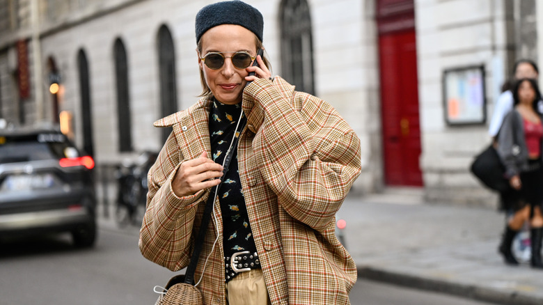 A woman with a black hat and a plaid coat with a straw bag