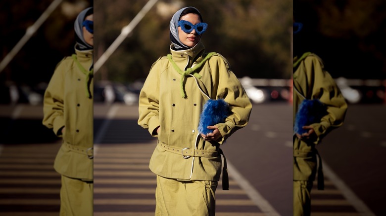 A woman with an olive green outfit and blue accessories photographed outside