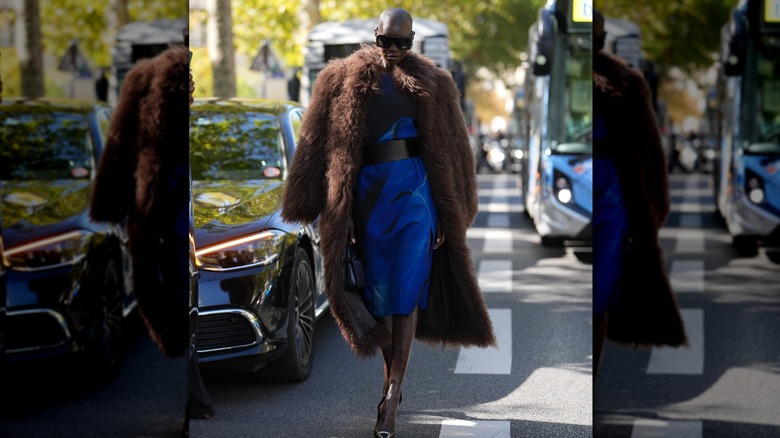 A woman wearing a big brown shaggy coat with a blue dress outside