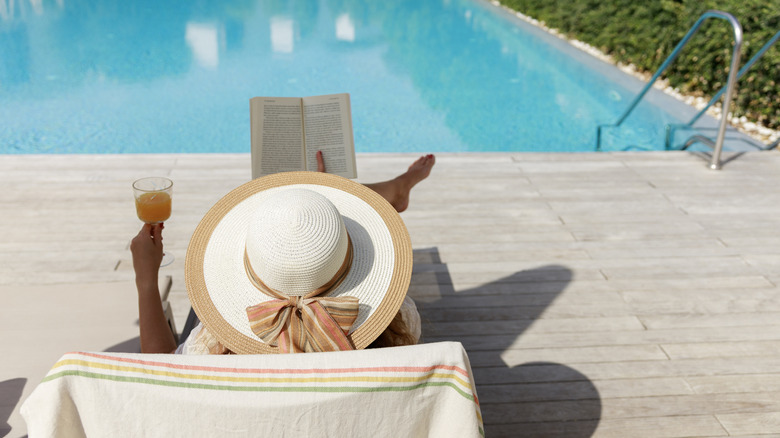 Woman reading book and drinking juice by poolside in summer