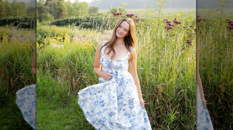 A girl smiles in a field wearing a blue-and-white floral dress