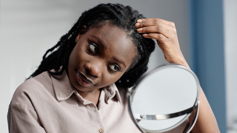 A woman touching her dreadlocked hair while looking in a mirror