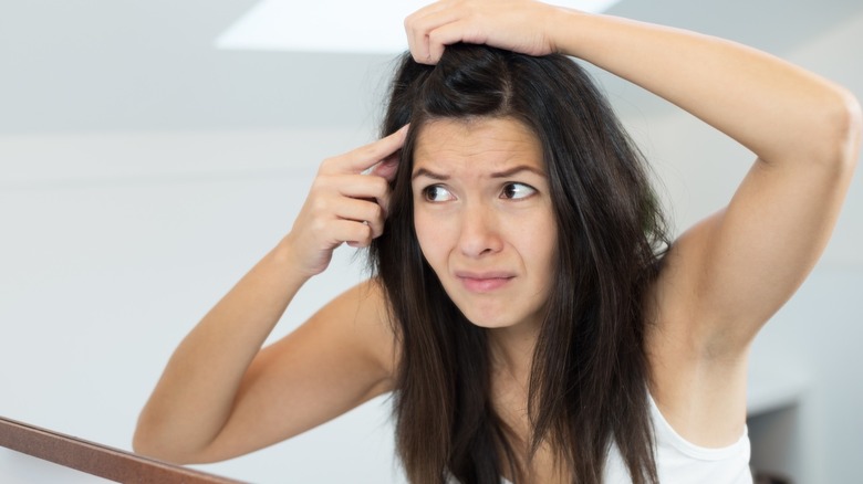 A woman touching her dark hair while looking in a mirror