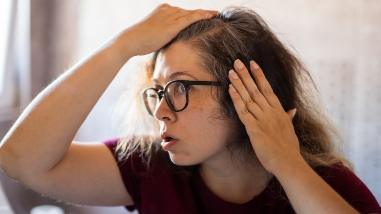 A woman lifting her hair to see her gray strands