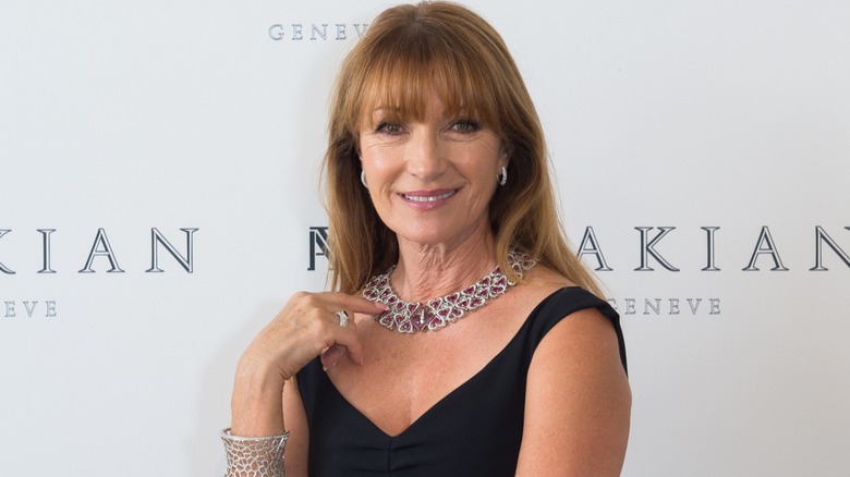 Jane Seymour smiling on the red carpet in a black dress in front of a white background