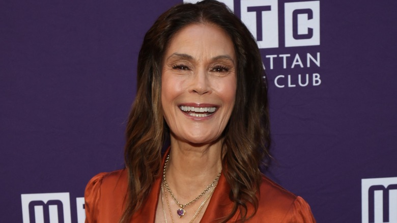 Teri Hatcher smiling on the red carpet while posing in front of a purple background