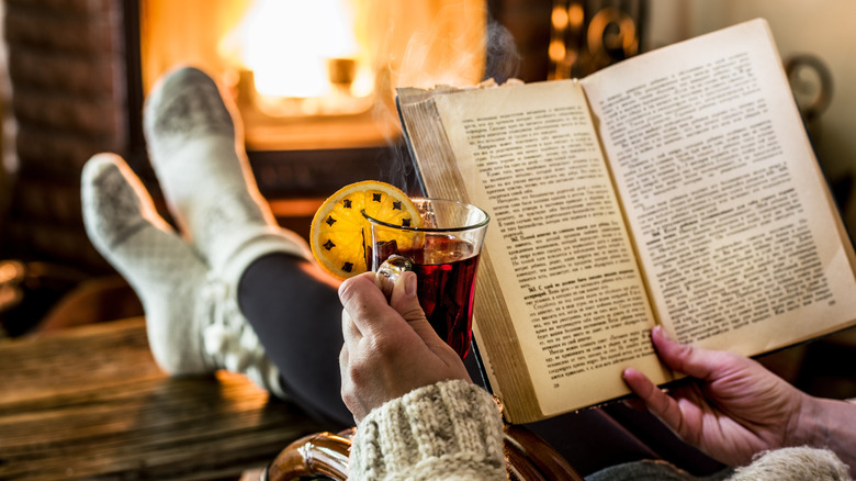 Woman reading a book while warming by cozy fireplace in winter day