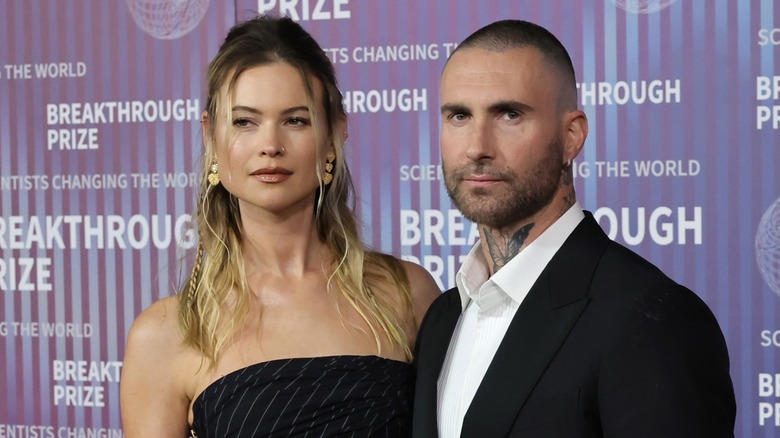 Behati Prinsloo posing with a neutral expression next to Adam Levine on the red carpet