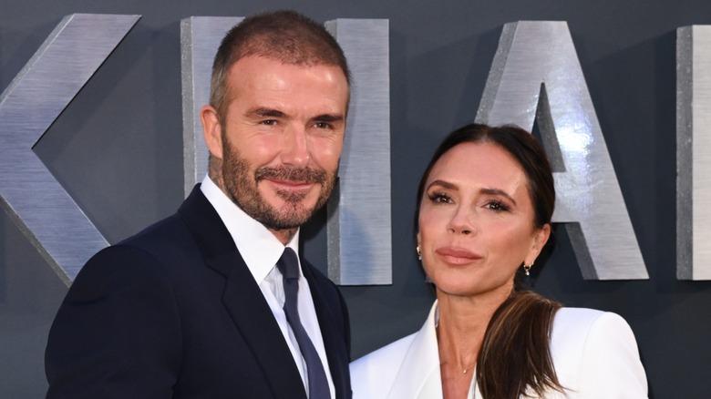 David Beckham slightly smiling next to Victoria Beckham with a neutral expression on the red carpet