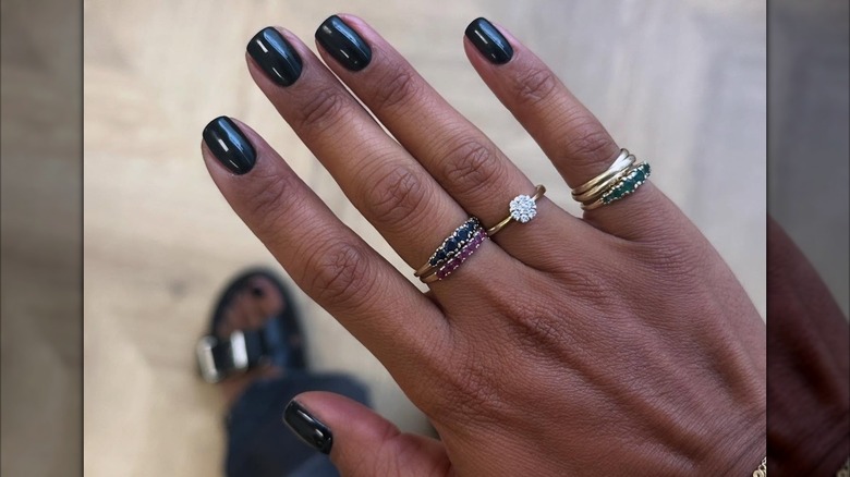 A woman's hand with several rings showing her short, black manicure