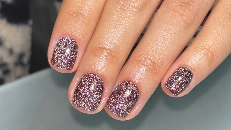 A woman's hand showing her brown glitter manicure on short nails