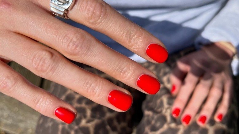 A woman's hands showing her short nails and a bright red manicure