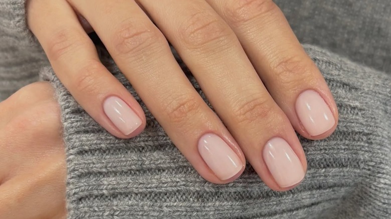 A woman's hand showing her nude manicure over a gray sweater