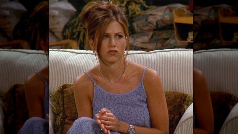 Rachel Green sitting on a couch and wearing a blue dress with spaghetti straps