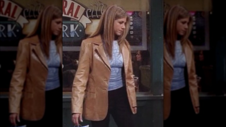 Rachel Green standing on the street wearing a blue tank top and a brown leather blazer