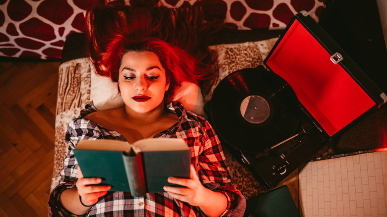 Woman with red hair reading a book next to a turntable
