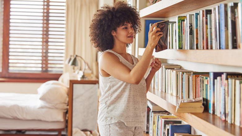 Woman holding  a mug and reading the back of a book in front of a large bookcase