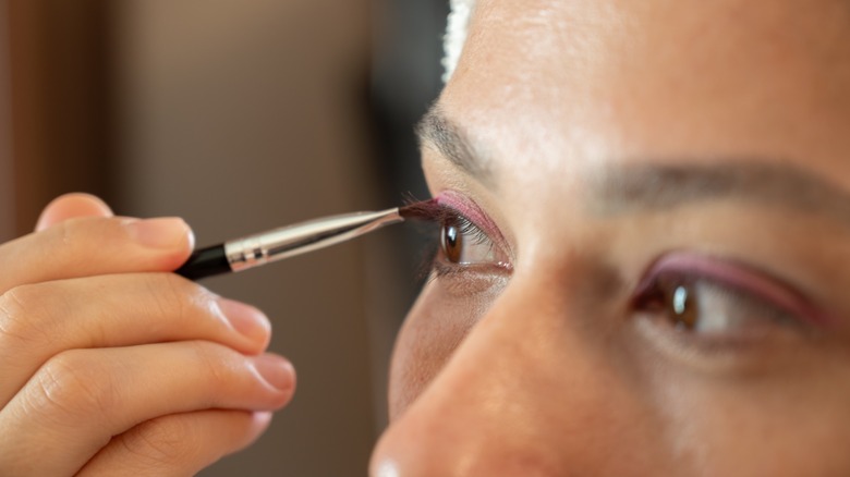 A woman applying pink eyeshadow to hooded eyes