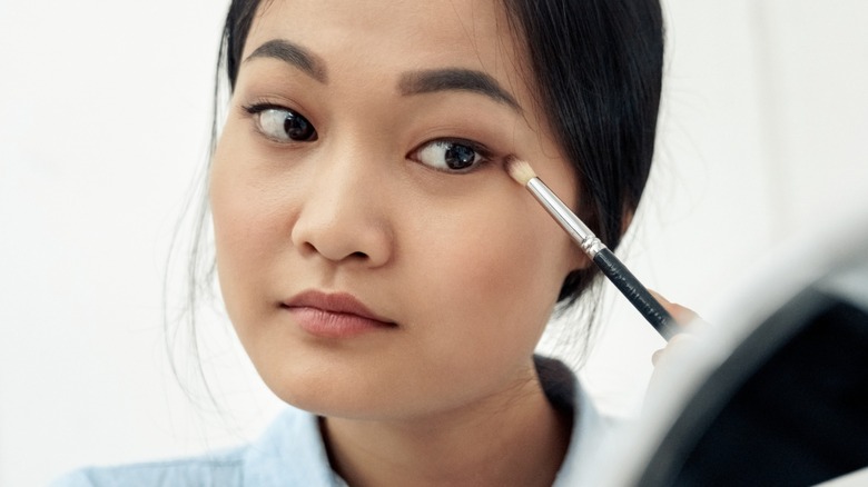 A woman applying eyeshadow to her eye with a small brush