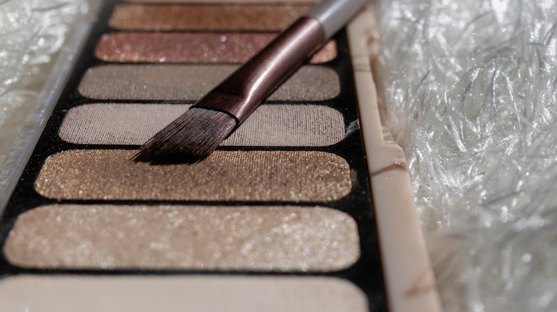 An eyeshadow palette containing shimmer shadow with a flat, angled brush hovering above it