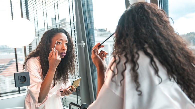 A woman applying eyeshadow with a brush while looking in a mirror