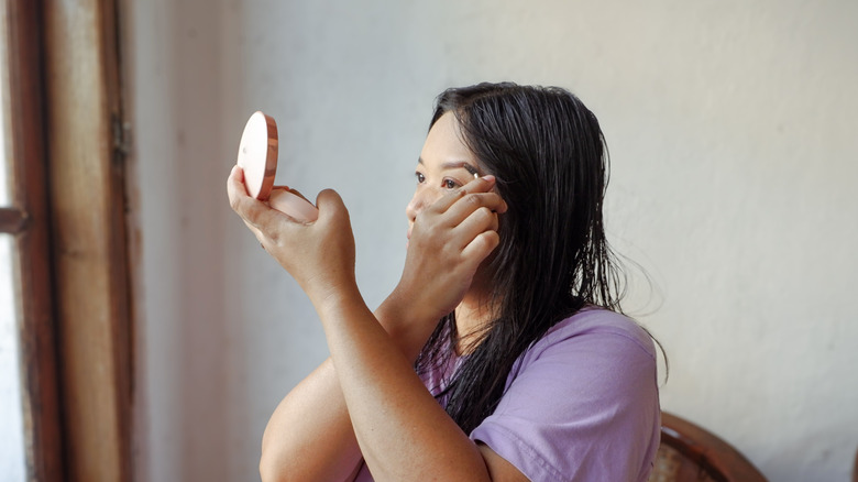 older women looking forward into small mirror wearing a pink shirt