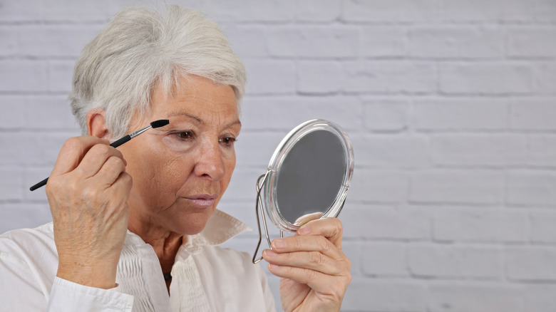 older women looking forward into small mirror wearing a white shirt