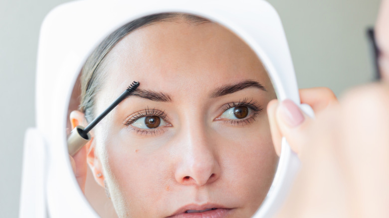 women looking white mirror and applying brow gel