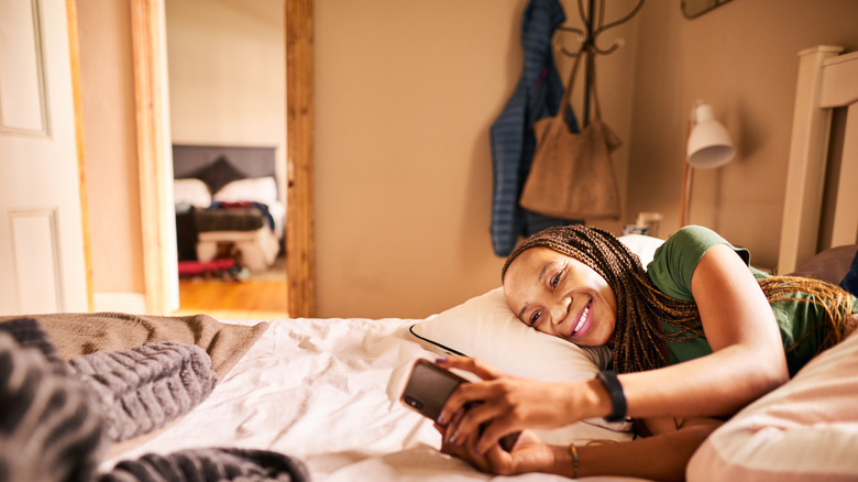 A woman with braids in her hair in bed on her phone