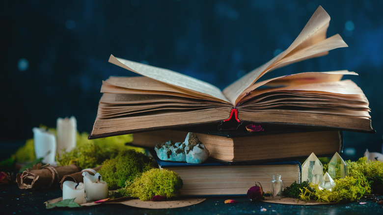 Stack of books with crystals, herbs, candles, and potion bottles