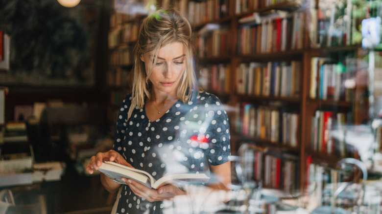 A woman inside the window of a bookstore and looking at a book