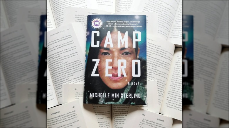 A copy of the novel "Camp Zero" on top of many open books