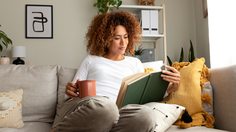 A woman sitting on a couch with coffee and reading a book