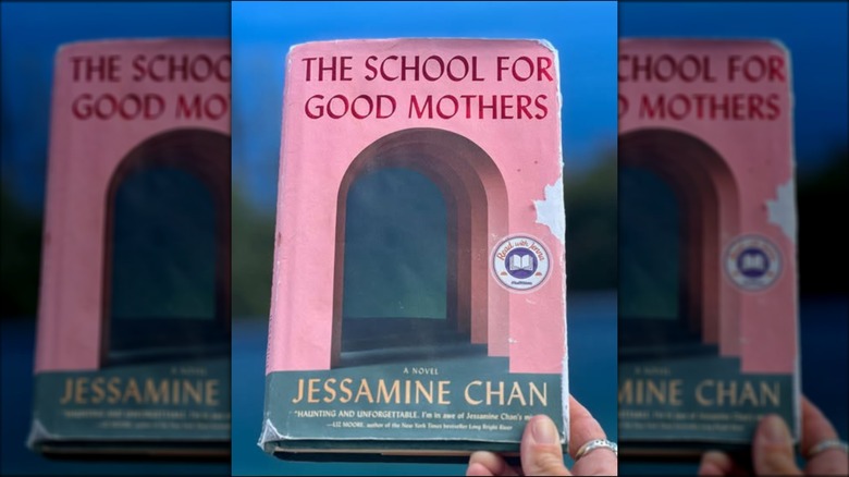 A hand holding up a copy of "The School for Good Mothers"