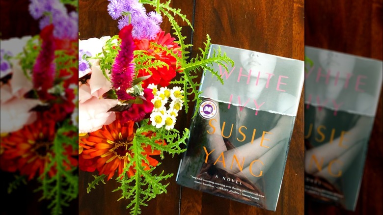A copy of the book "White Ivy" on a table next to a vase of flowers