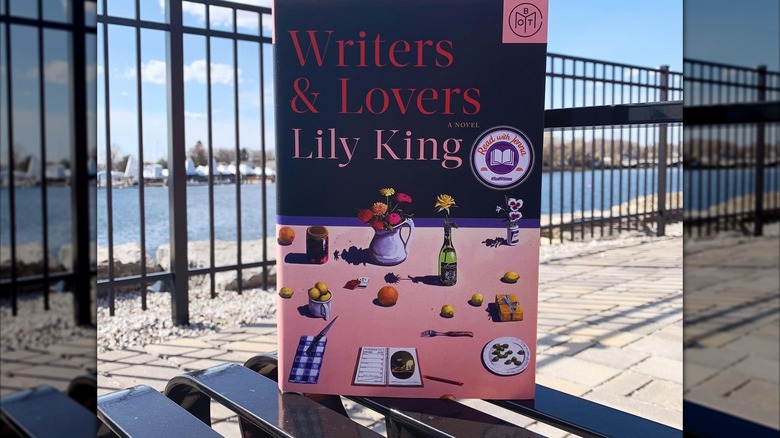 A copy of the novel "Writers & Lovers" on an iron table with beach, fence, and water in the background