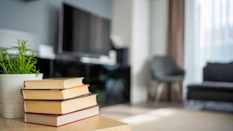 Book stack sitting on coffee table next to potted plant with a flat screen TV visible in the background