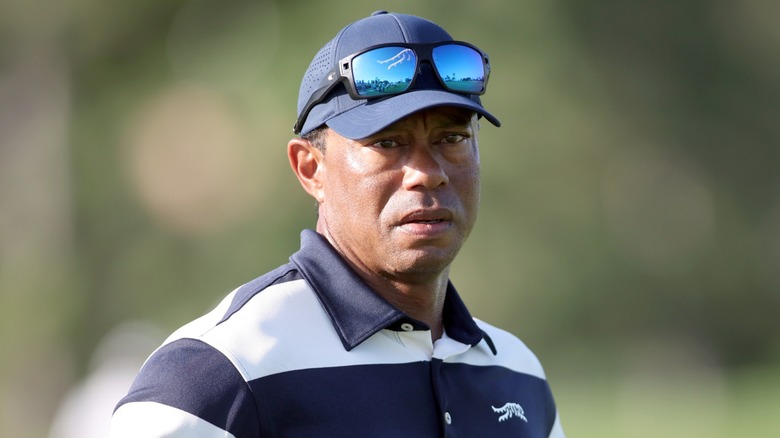 Tiger Woods with a serious expression and wearing a baseball cap on the golf course